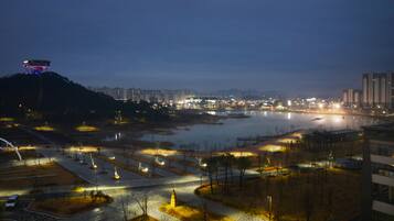 A nighttime view of a cityscape with a river, illuminated pathways, and buildings.
