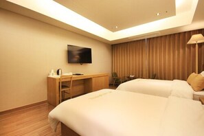 Ein Hotelzimmer mit zwei Betten, einem Schreibtisch, einem Fernseher und einem fensterbepflanzten Fenster.