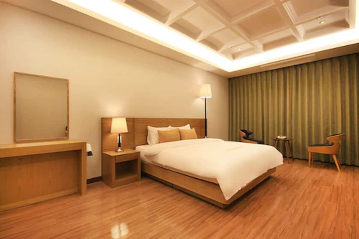 A hotel room with a large bed, a bedside table, a lamp, a chair, and a mirror.