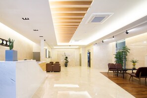 Eine moderne Hotelhalle mit einer Rezeption, einer Sitzecke und einer großen Pflanze.
