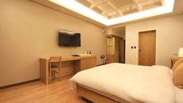 Una habitación de hotel con cama, escritorio, silla, televisor y puerta.