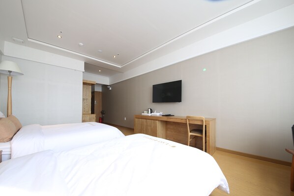 Habitación de hotel con dos camas, un escritorio, una silla, un televisor y una lámpara.