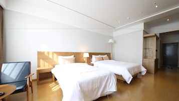 Camera d'albergo con due letti, una scrivania in legno, una sedia, un comodino e una lampada.