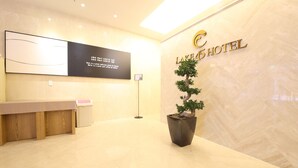 Un área de recepción con mostrador, un bonsái en maceta y un cartel en la pared con el nombre del hotel.
