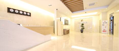A modern hotel lobby with a wooden staircase, a reception desk, and a sign for the lobby area.