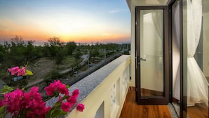 A balcony with a view of a sunset, a wooden floor, and a glass door. - Stayzi Hotel (Da Nang)