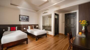 A hotel room with two beds, a desk, a chair, a door, and a picture on the wall.