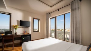 A hotel room with a bed, a desk with a computer, a TV, and a view of the city. - Stayzi Hotel (Da Nang)