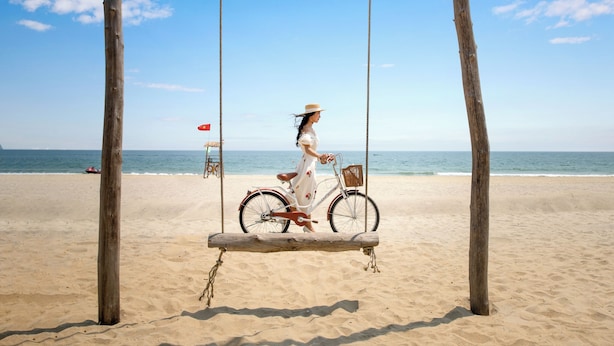 A beach scene with a wooden swing and a bicycle. - Stayzi Hotel (Da Nang)