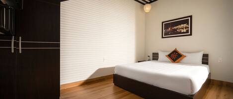 Un dormitorio moderno con una cama grande, suelo de madera, techo inclinado con vigas negras y un cuadro de paisaje urbano en la pared.