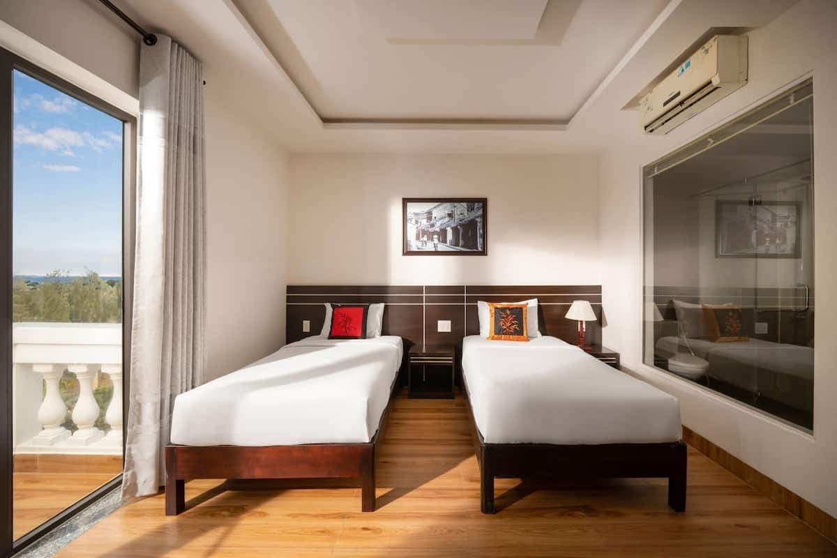A hotel room with two beds, a large window, and a view of the outdoors.