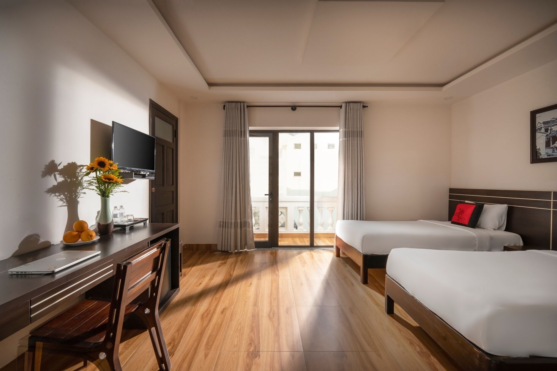 Ein Hotelzimmer mit Holztisch, Fernseher, zwei Betten und einem Balkon mit Vorhängen.