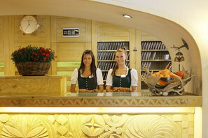 A reception desk with a clock, a basket of flowers, and a fruit basket. - Petit Steffani (St. Moritz)