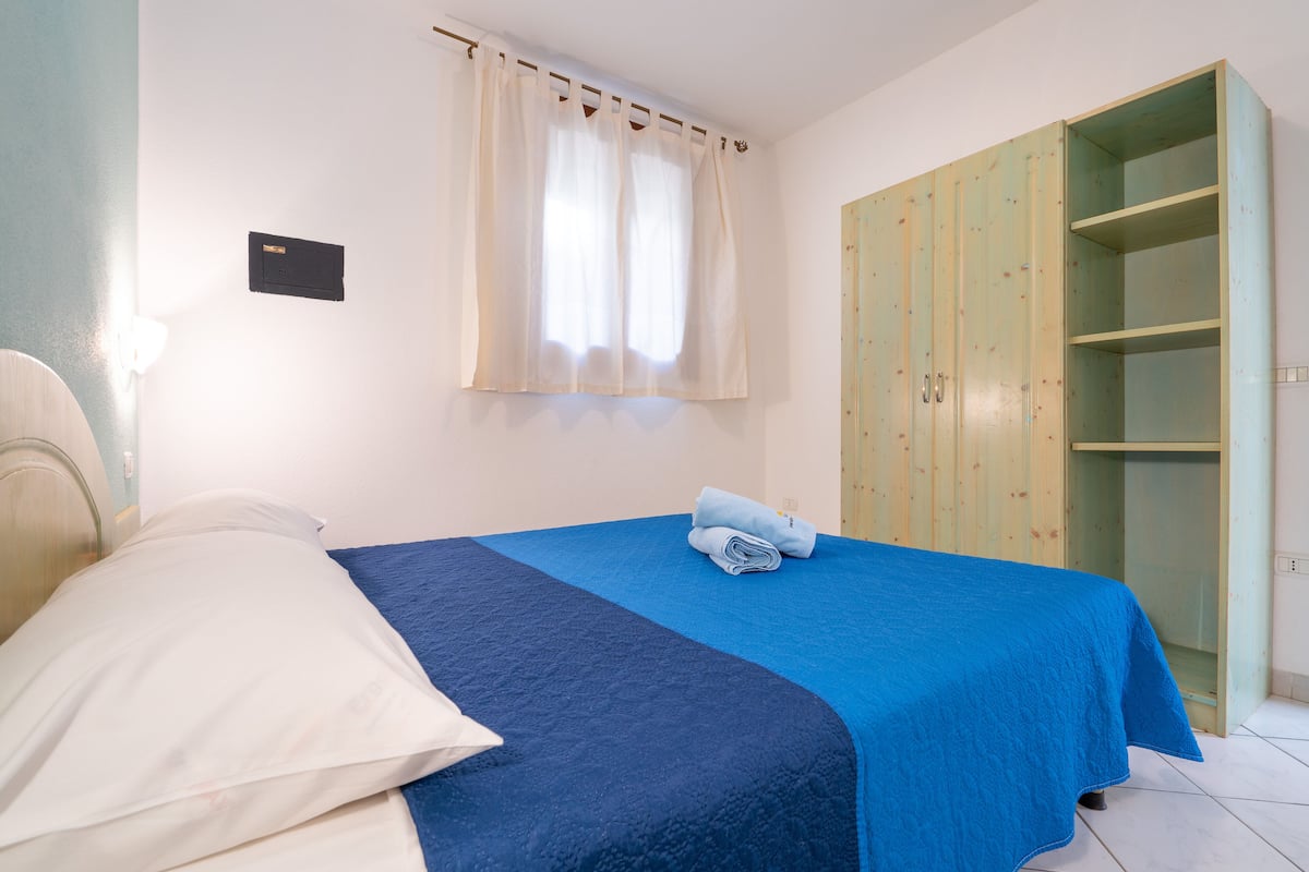 Ein Schlafzimmer mit Bett, Kleiderschrank und einem Fenster mit Vorhängen.