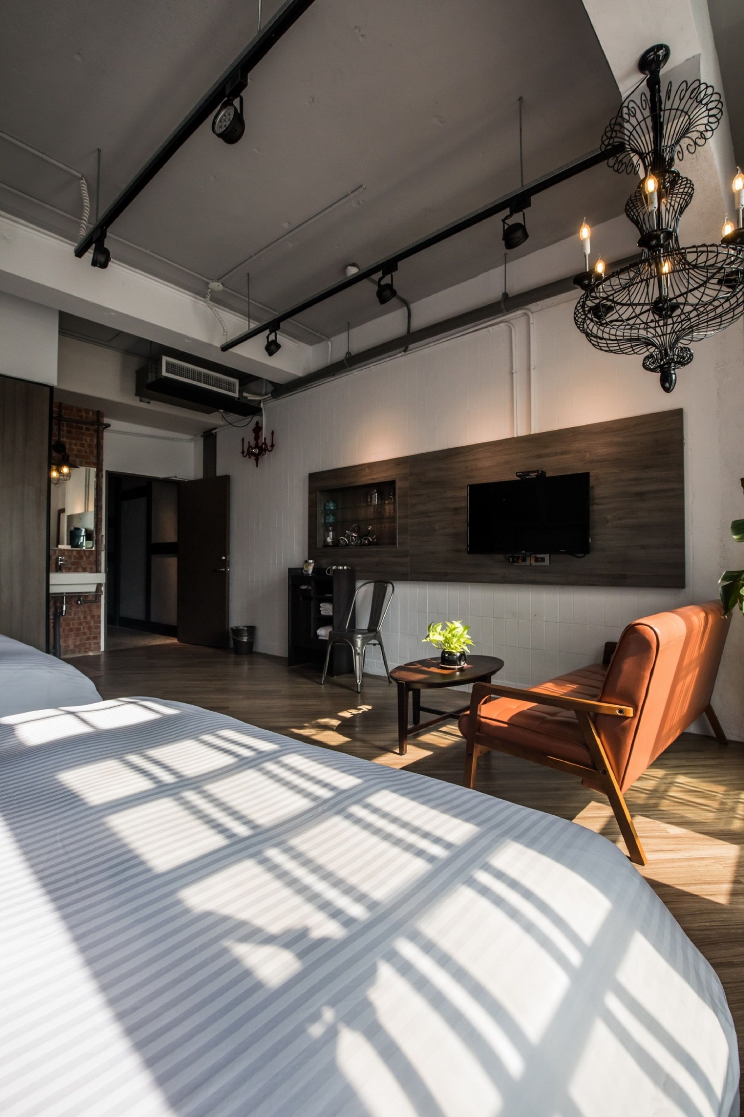 A modern bedroom with a large bed, a TV mounted on the wall, and a chandelier.
