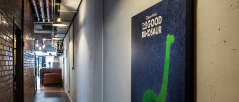 Un couloir avec une affiche du film « Le Bon Dinosaure » accrochée au mur, un mur de briques sur la gauche et un plancher en bois.