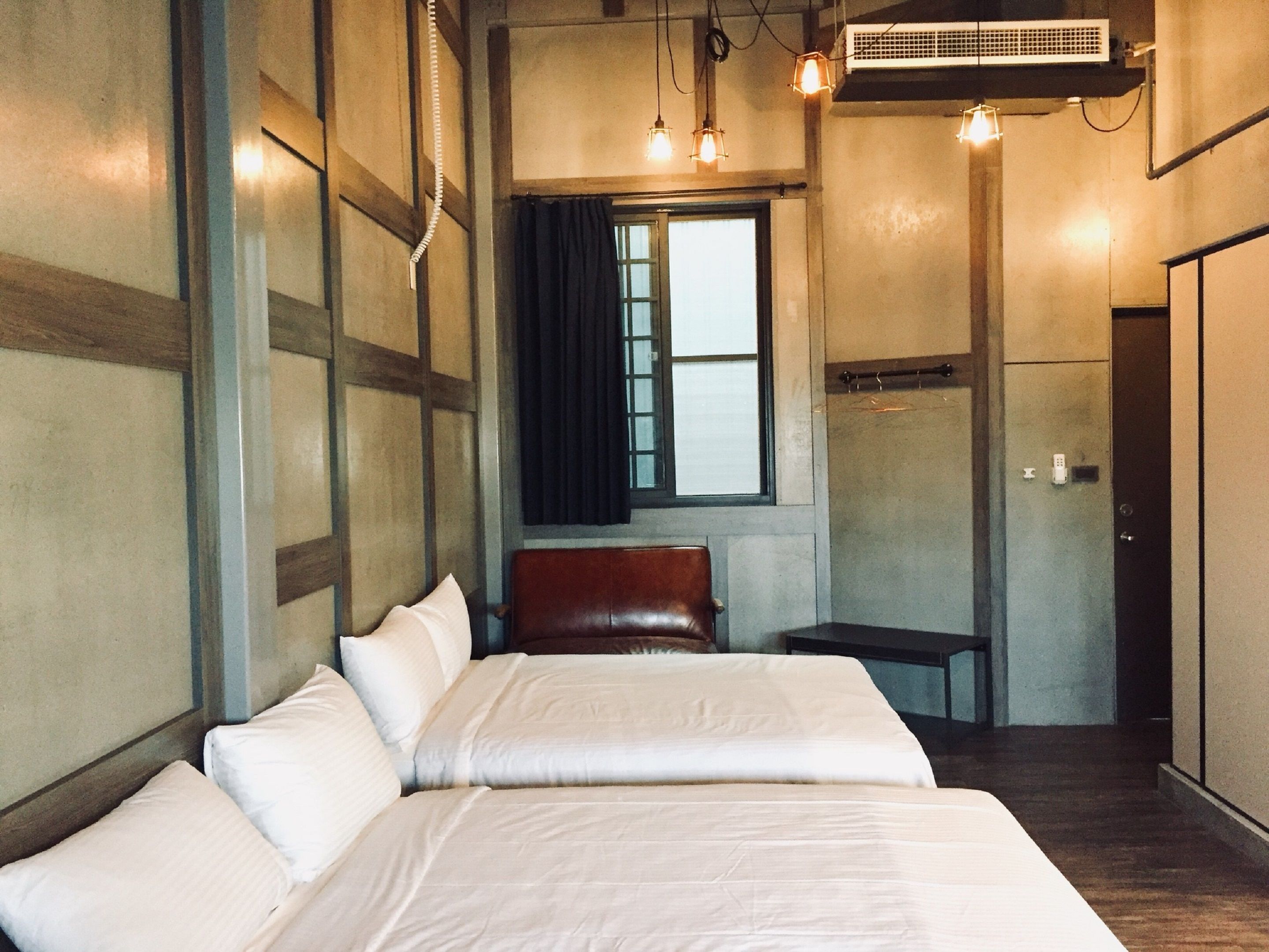 A hotel room with a large bed, a bench, a window, and an air conditioning unit.