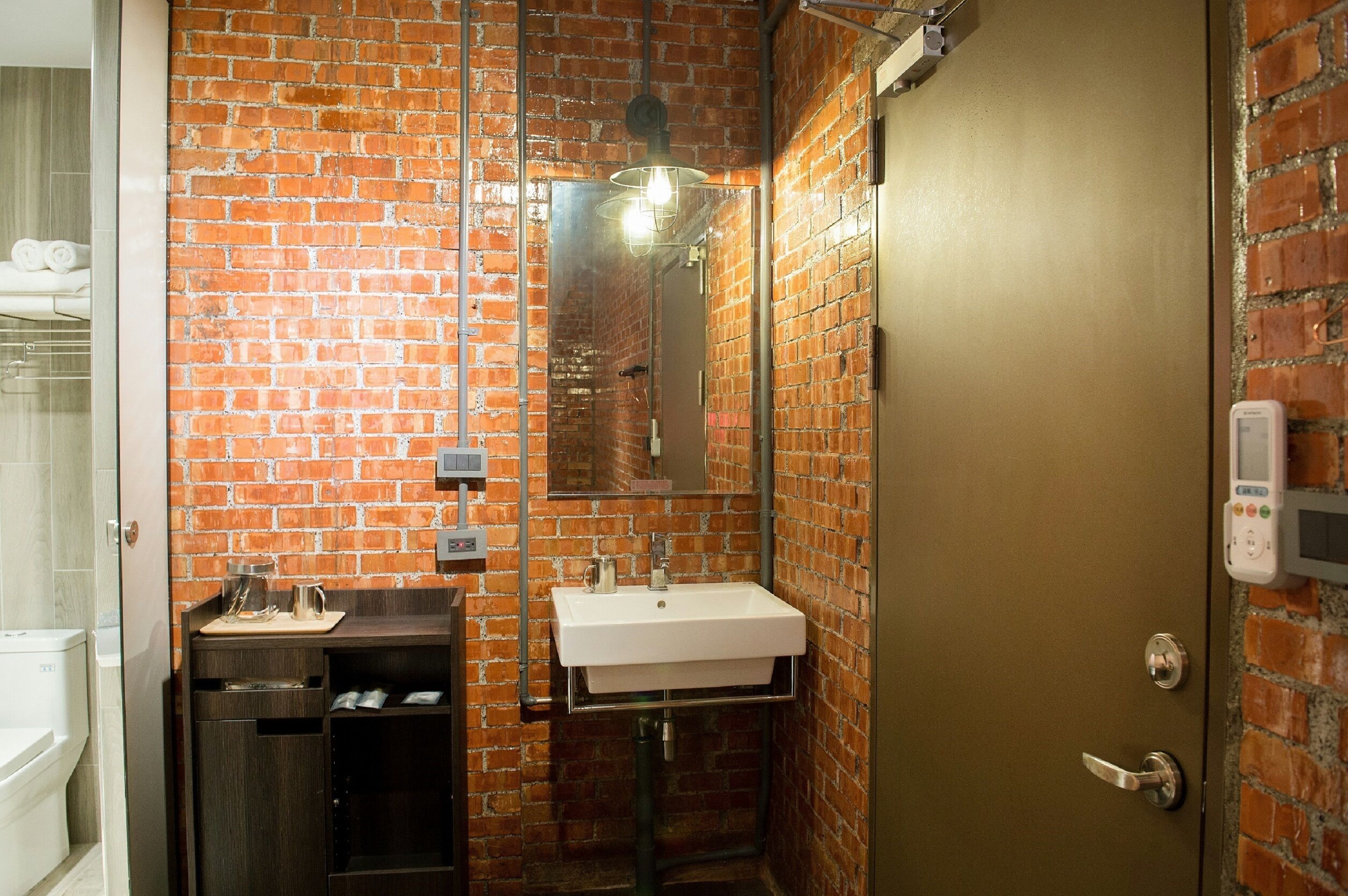 A bathroom with a brick wall, a white sink, a mirror, and a shower.