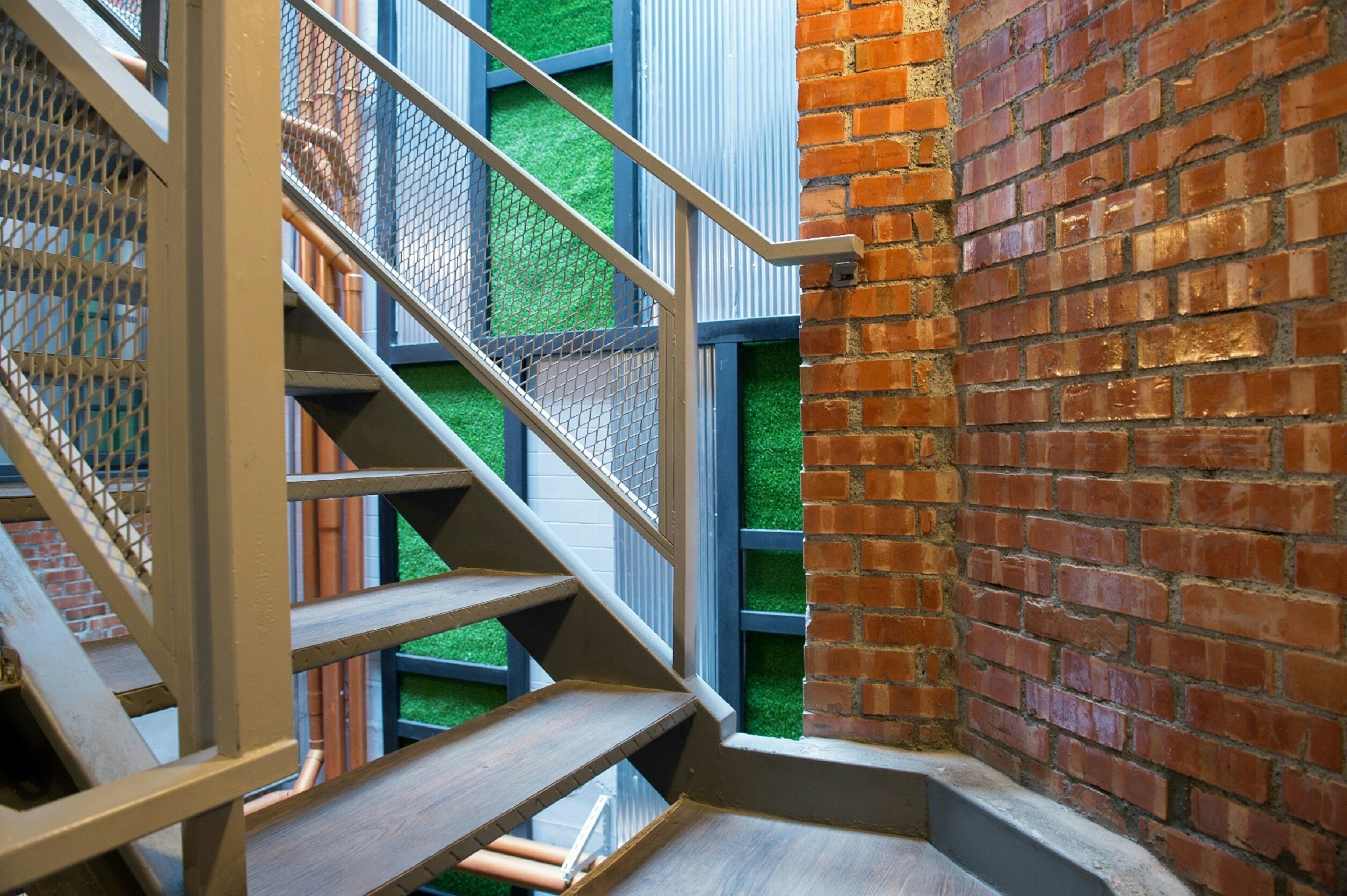A staircase with metal railings and wooden steps leading to a green-tiled area.