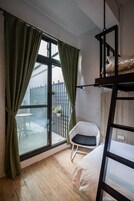 Una habitación con literas, una mesita con sillas y vistas al exterior a través de un amplio ventanal con cortinas.