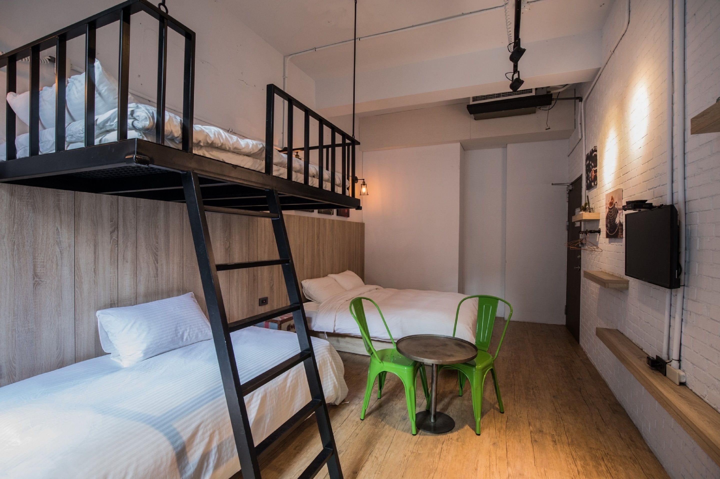 A dorm-style room with bunk beds, a small table with chairs, a TV, and a wooden wall.