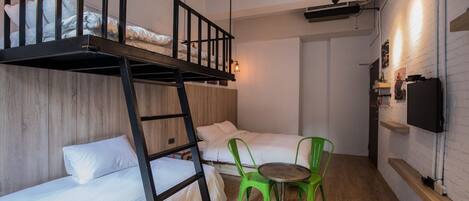 A dorm-style room with bunk beds, a small table with chairs, a TV, and a wooden wall.