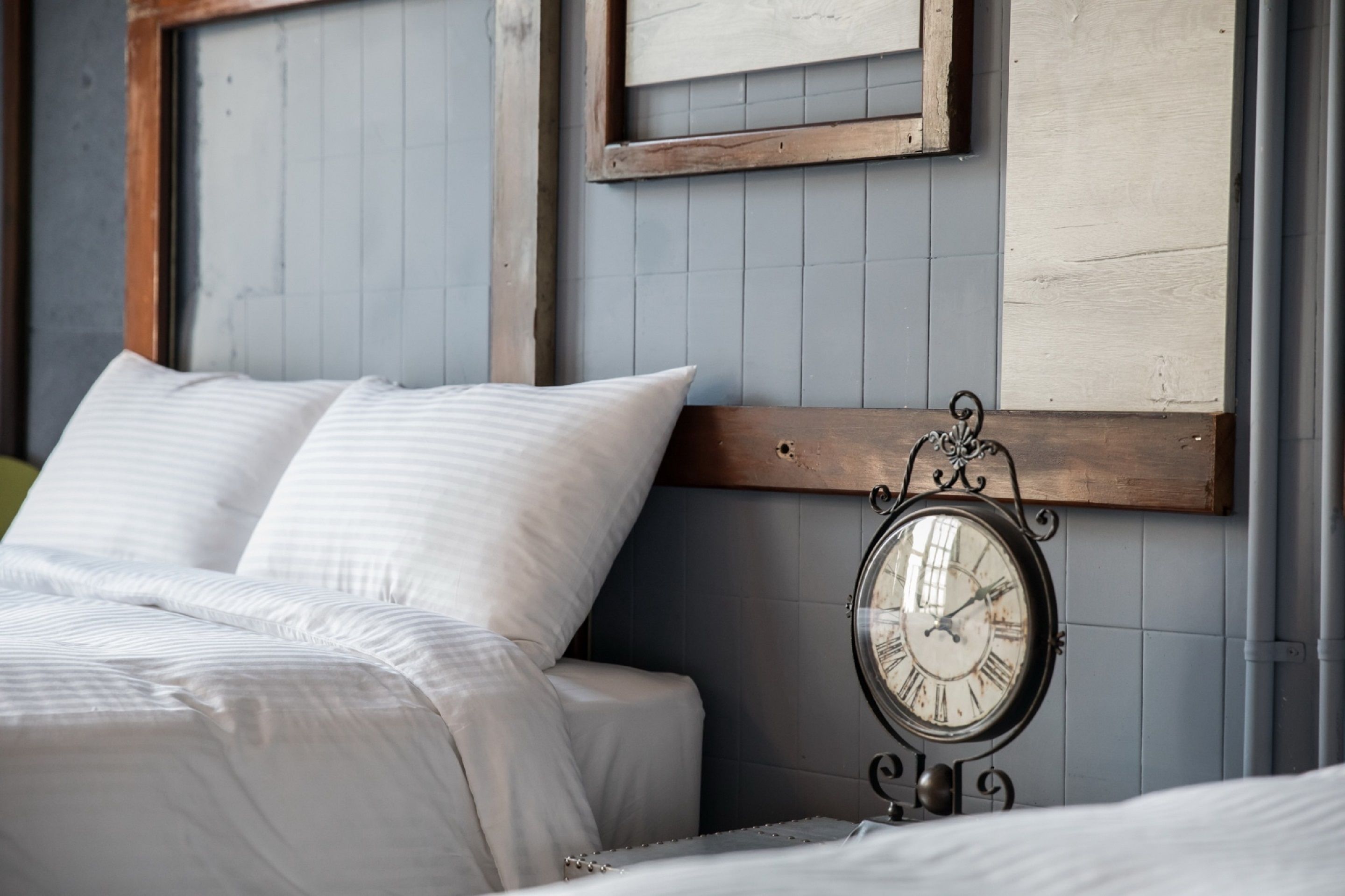 A neatly made bed with white linens and a wooden headboard against a tiled wall.