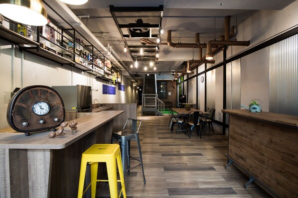 A modern bar area with a wooden counter, stools, and a retro clock.