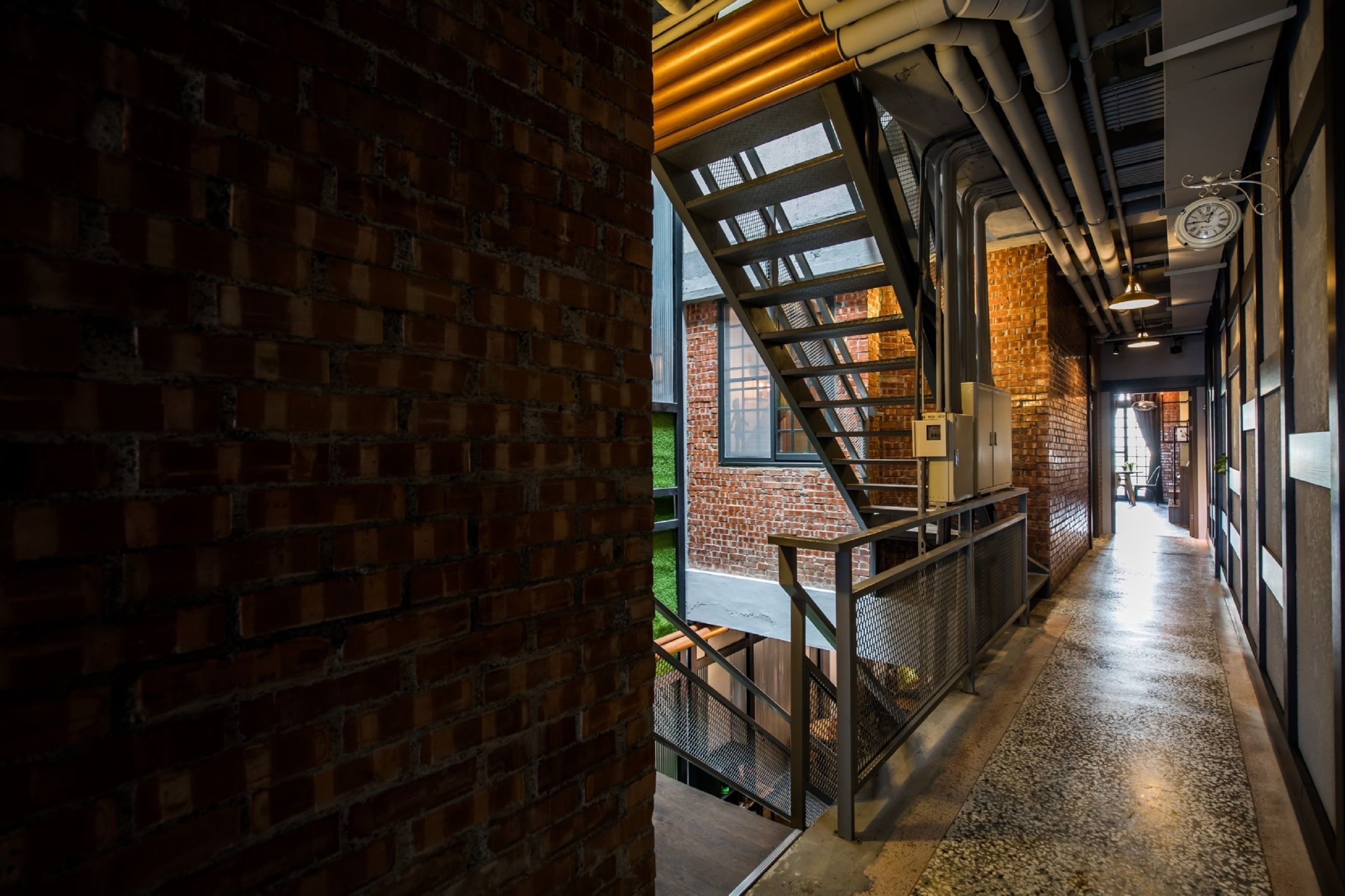 A corridor with exposed brick walls, a metal staircase, and a concrete floor.