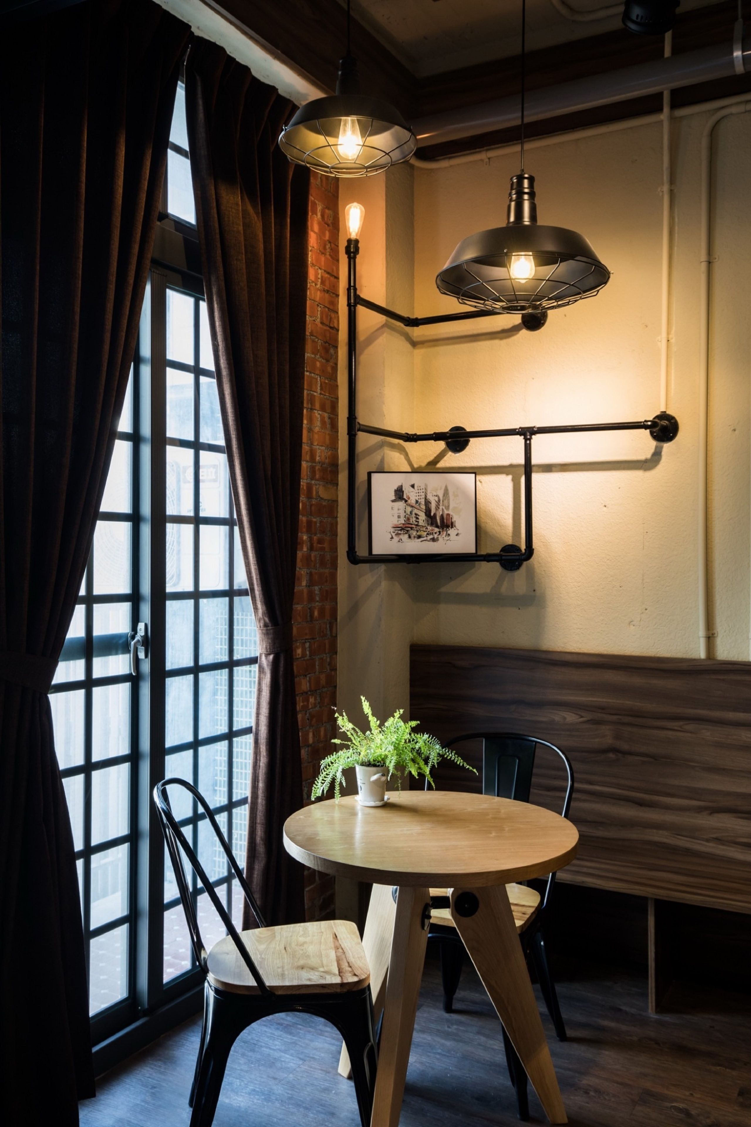 A dining area with a round wooden table, two chairs, a potted plant, and a hanging light fixture.