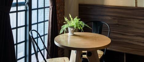 A dining area with a round wooden table, two chairs, a potted plant, and a hanging light fixture.