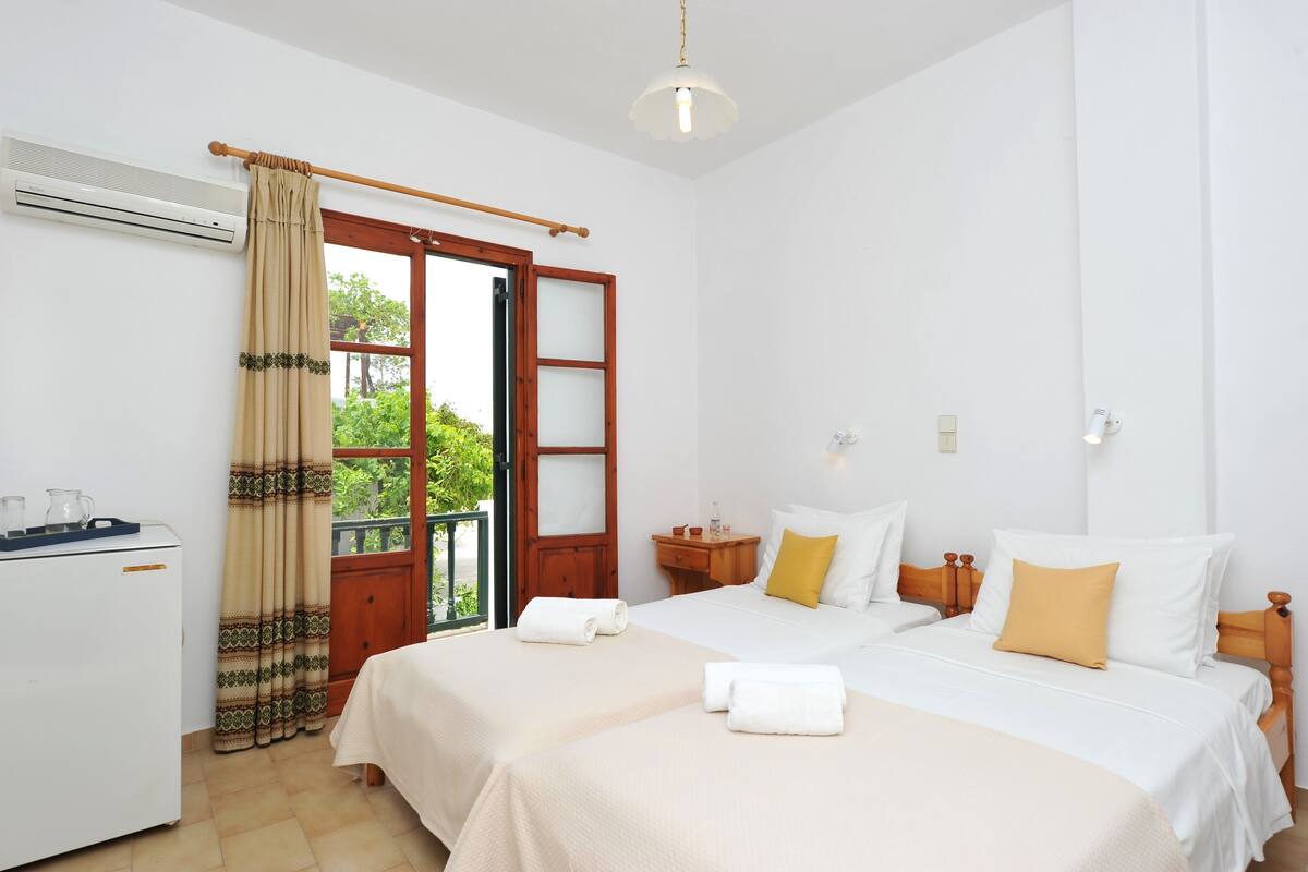 A hotel room with two beds, a small desk, and a window with a view of greenery.