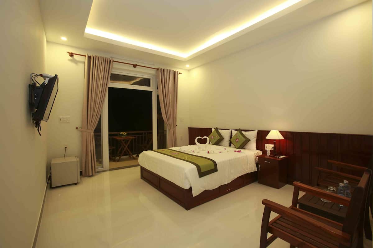 Habitación de hotel con cama, escritorio, silla, lámpara y vistas al exterior.
