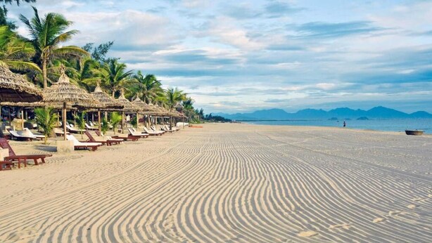 Ein Strand mit strohgedeckten Hütten und Liegestühlen entlang der Küste.