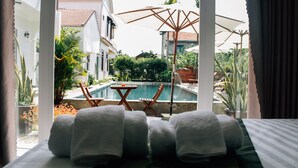 Ein Hotelzimmer mit Blick auf einen Swimmingpool, Sitzgelegenheiten im Freien und einem Balkon mit Pflanzgefäßen.