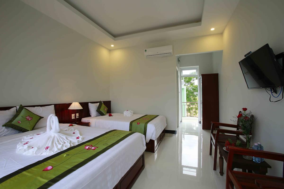 Habitación de hotel con dos camas, un televisor montado en la pared y una zona de comedor con mesa y sillas.