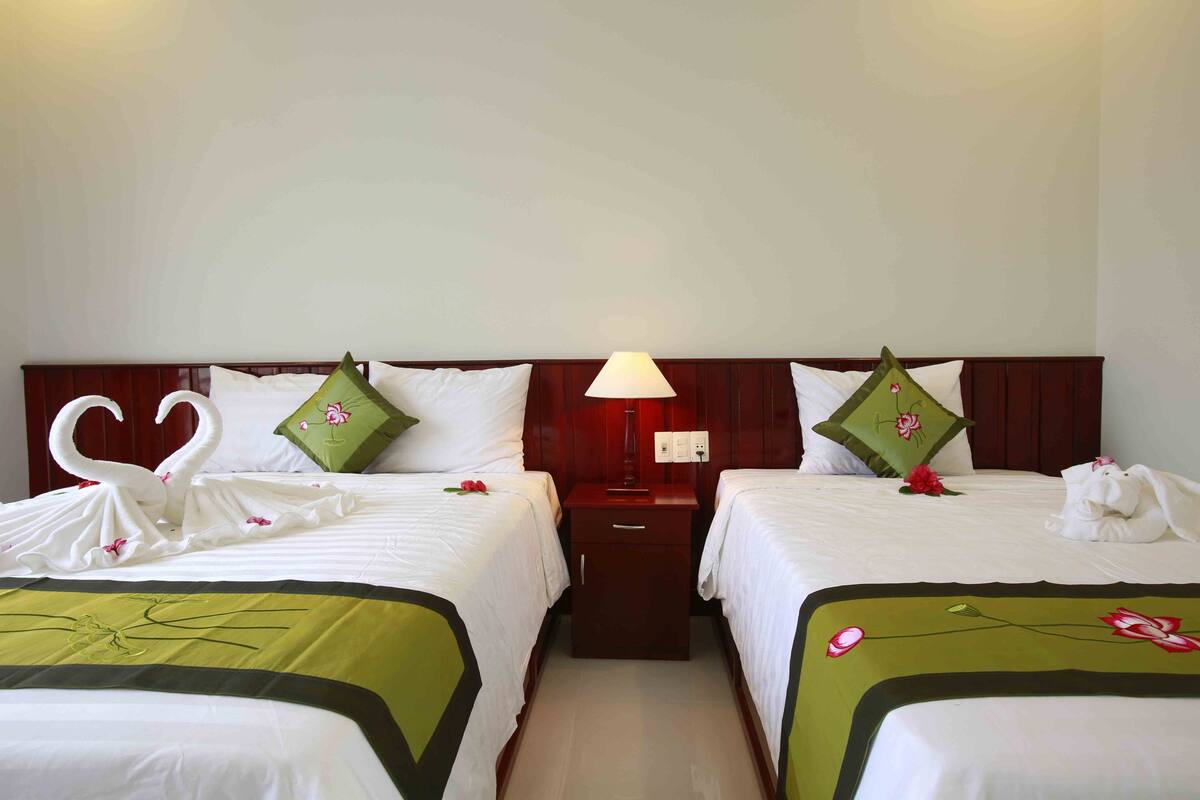 Habitación de hotel con dos camas, cada una con cubrecama verde y blanco, cabeceros de madera y una mesita de noche entre ellas.