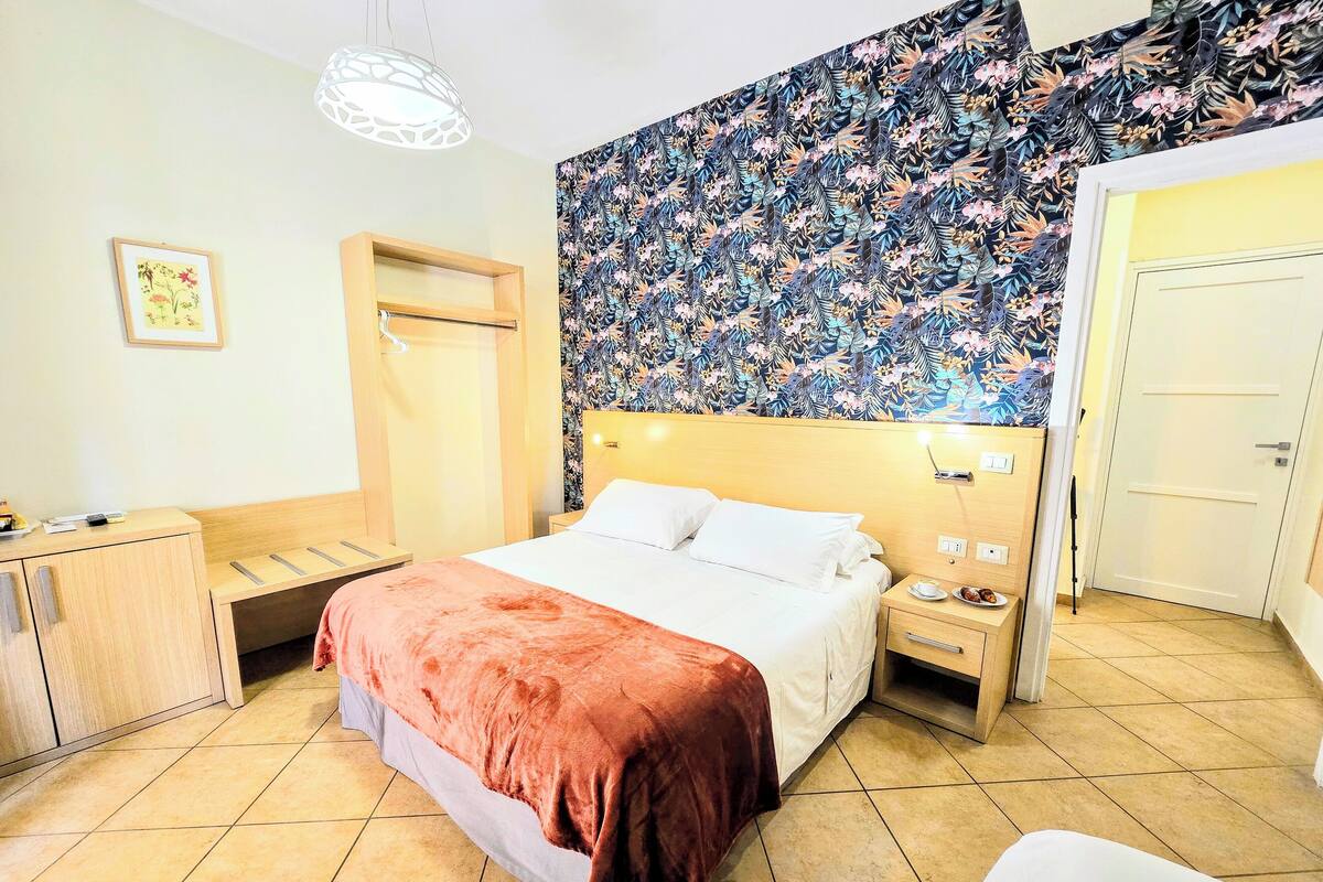 Ein Hotelzimmer mit Bett, Nachttisch und einer Wand mit floralem Muster.