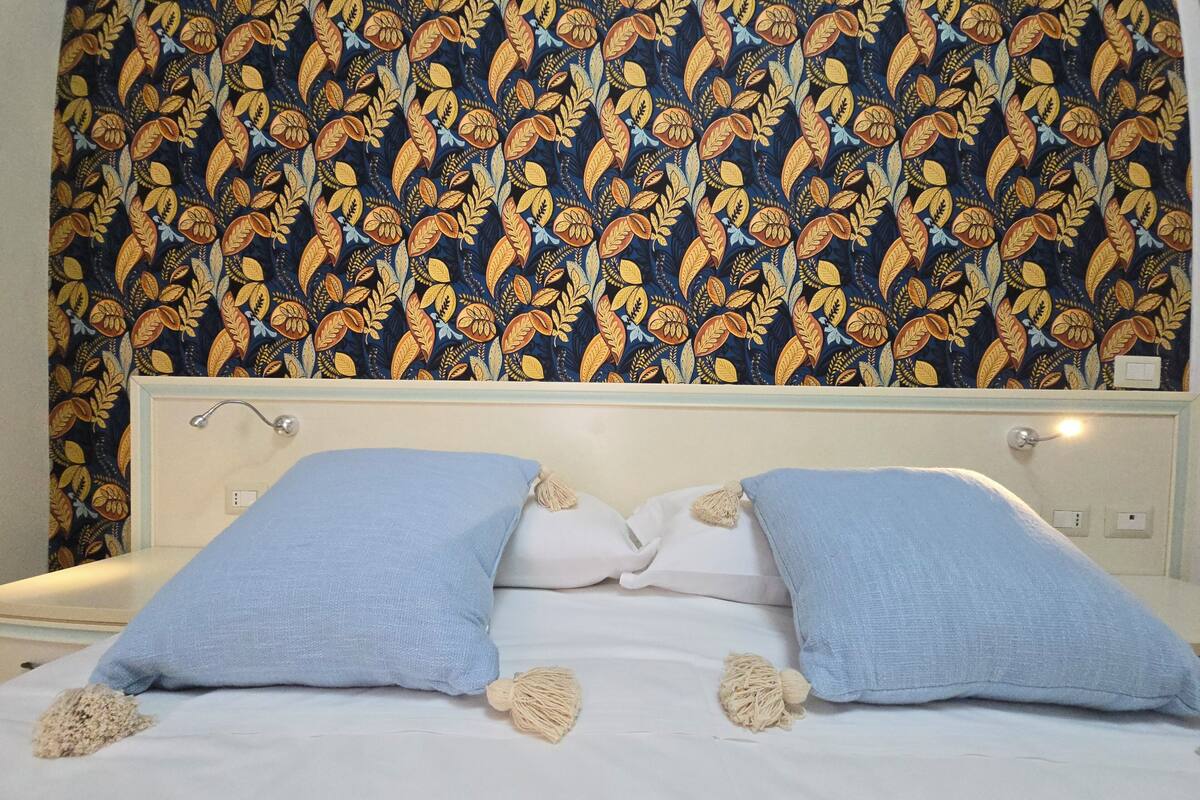 Ein Bett mit zwei blauen Kissen und einem weißen Kissen vor einer Wand mit blumigem Wandpapier.