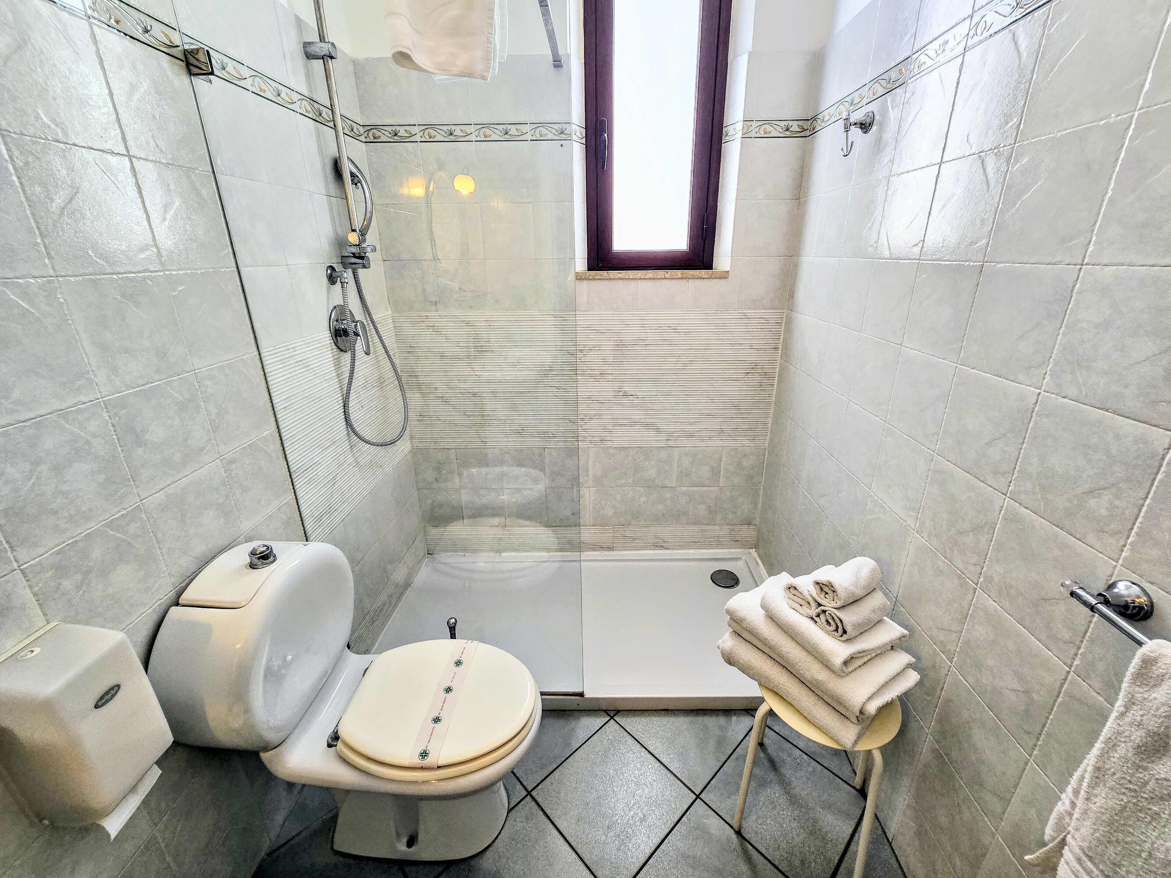 Un baño con inodoro, ducha y una pequeña mesa con toallas.