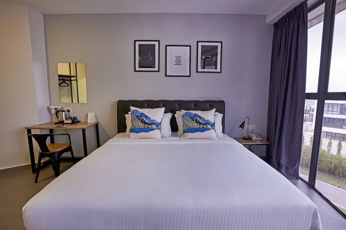 A hotel room with a large bed, a desk, a chair, and a view of the city through the window.