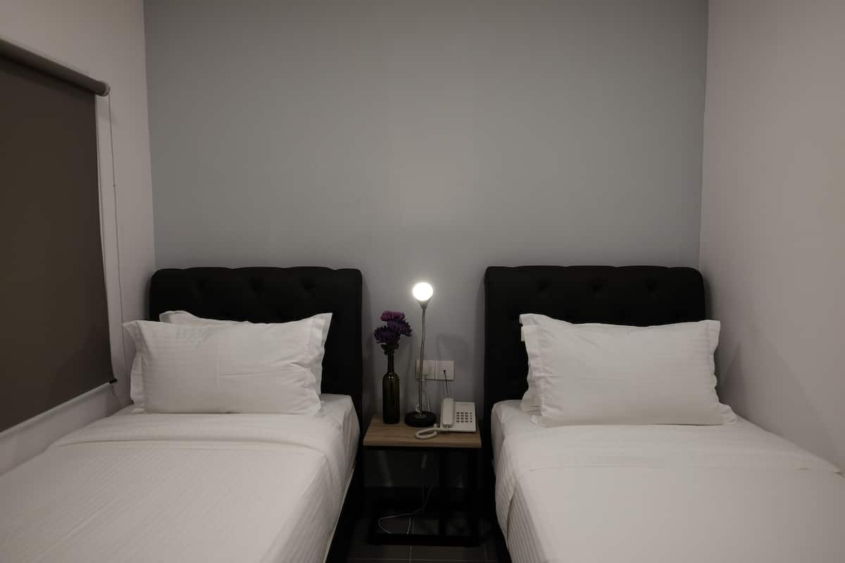 A small, dimly lit room with two single beds, a nightstand with a lamp, a vase with flowers, and a phone.