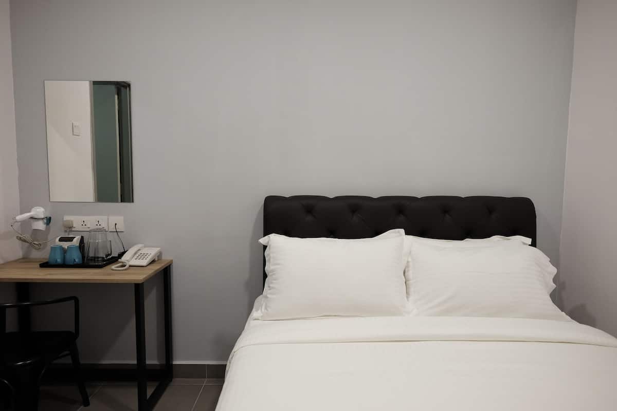 A hotel room with a bed, a bedside table with a phone, a lamp, and a mirror.