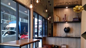 Un interno moderno con una reception in legno, sgabelli da bar e una panca. Sono presenti luci pendenti, un cartello con scritto 'WELCOME' e uno scaffale con oggetti decorativi.