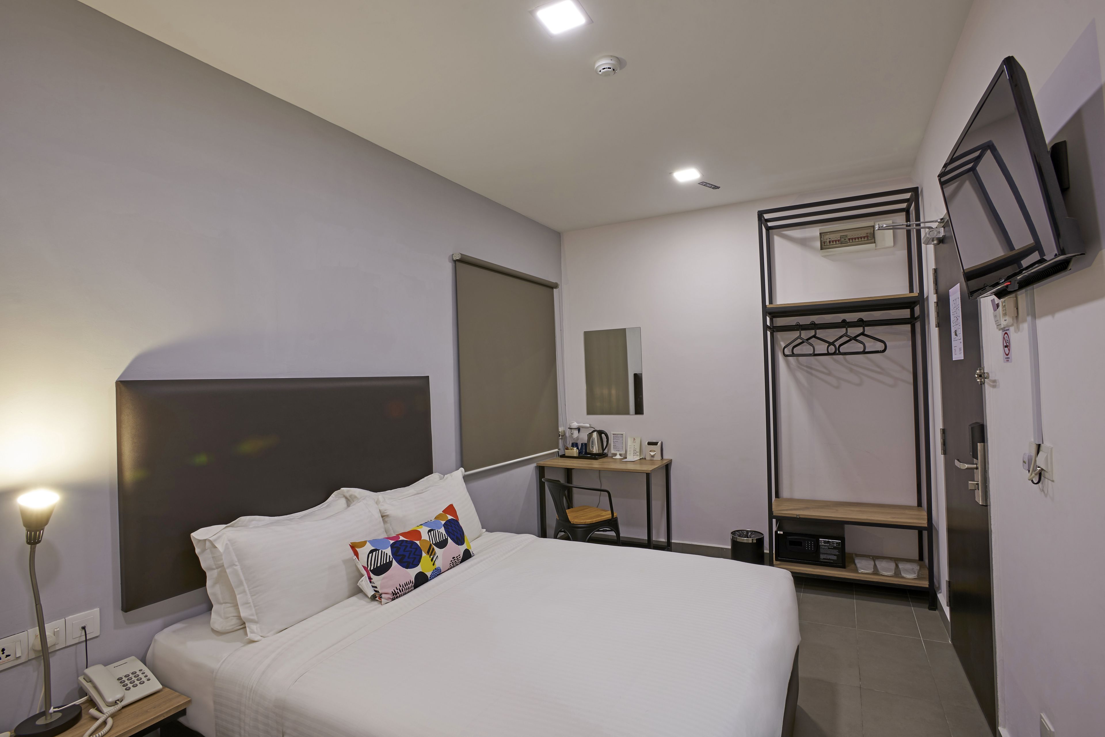 A hotel room with a bed, bedside table, desk, chair, TV, and wardrobe.