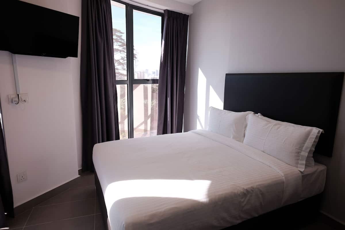 A hotel room with a bed, a TV mounted on the wall, and a window with curtains.