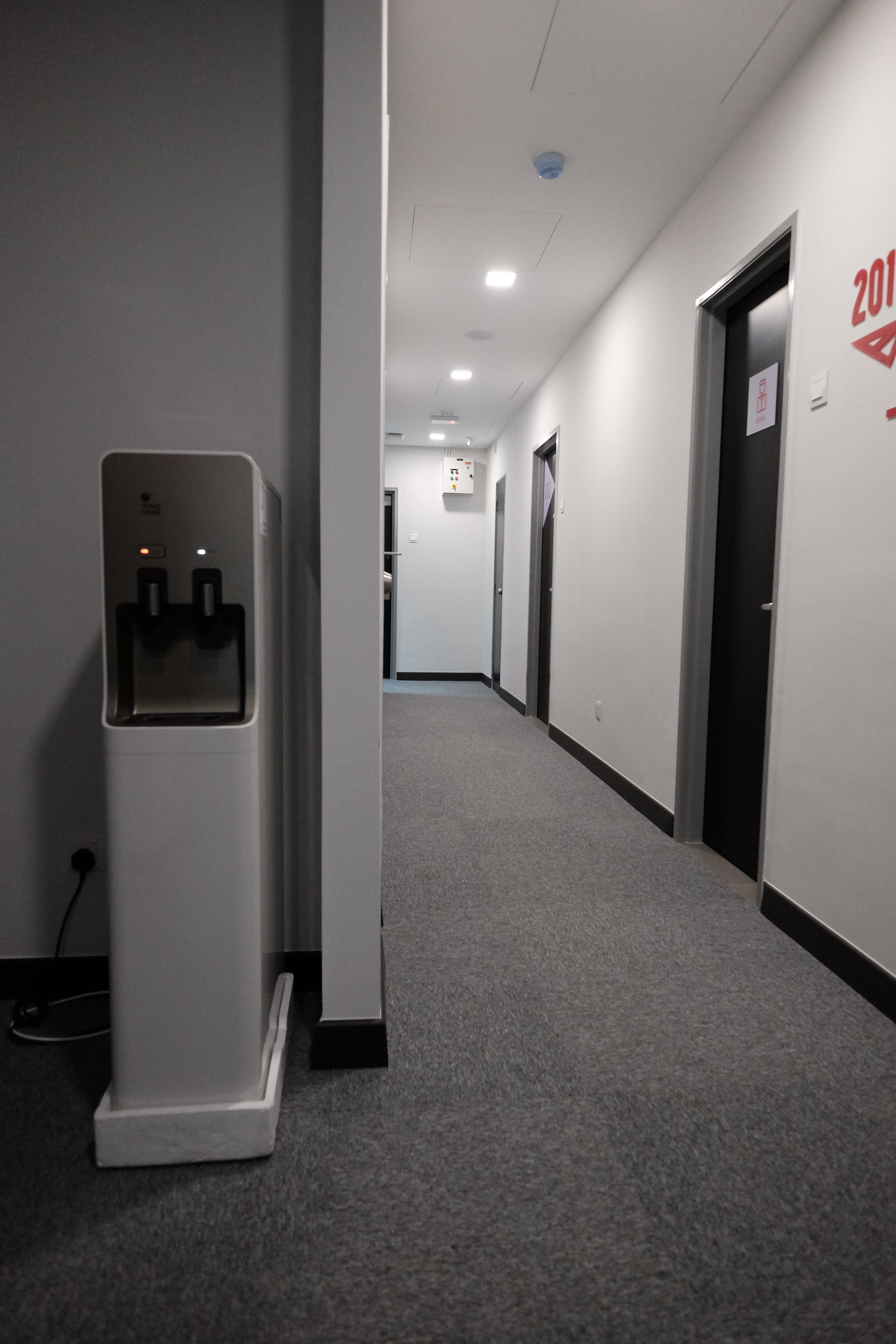 A hallway with a water dispenser, a fire alarm, and a door marked with the year 2011.