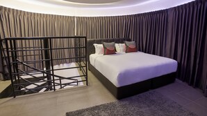 Una camera da letto moderna con soffitto curvo, un letto con biancheria bianca e numerosi cuscini, una scala in metallo nero e un pannello decorativo grigio.