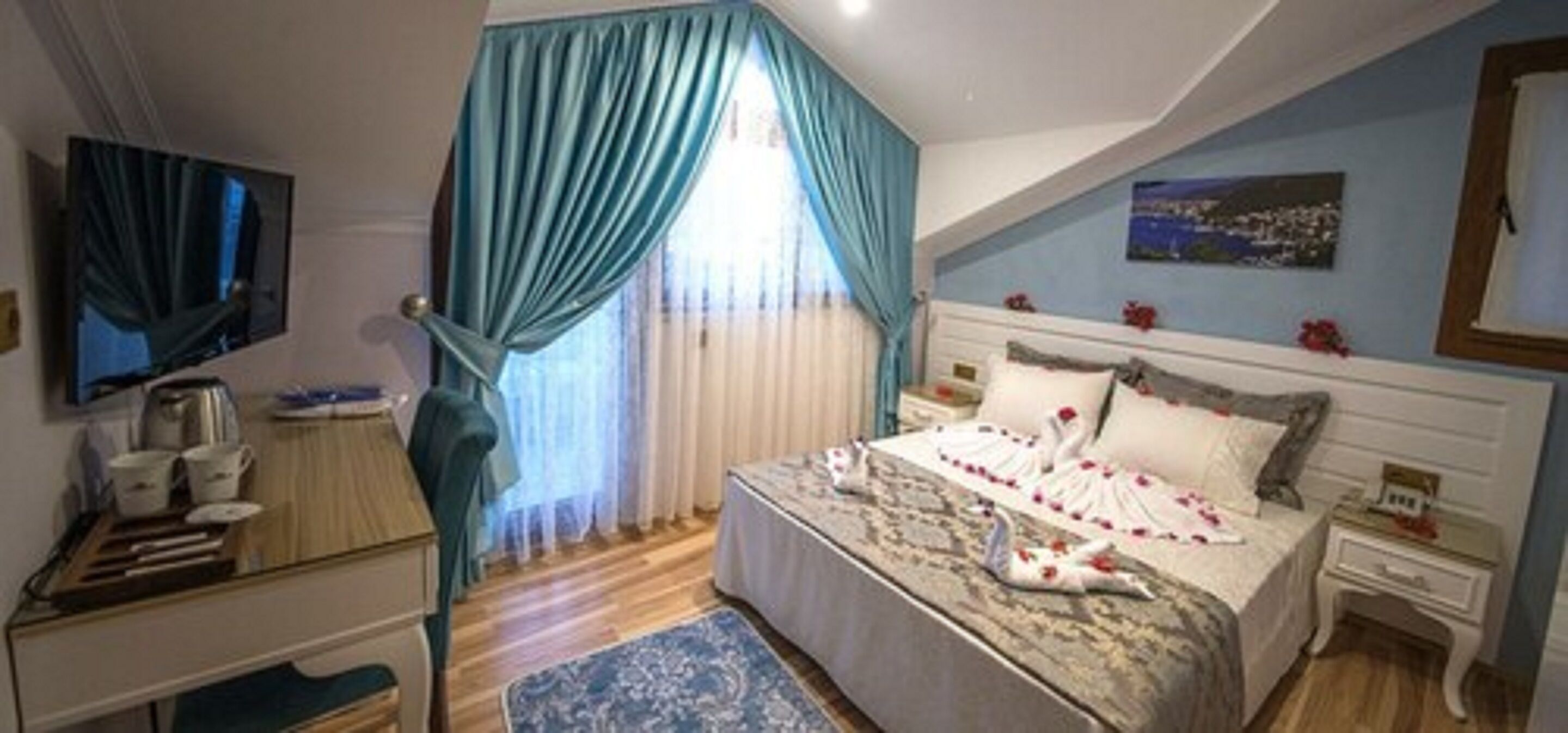 Een slaapkamer met een bed, een televisie, een bureau en een raam met gordijnen.