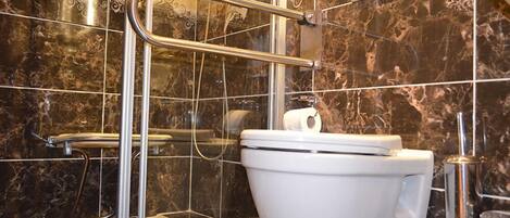 A modern bathroom with a glass shower enclosure, a white toilet, and a marble-tiled wall.